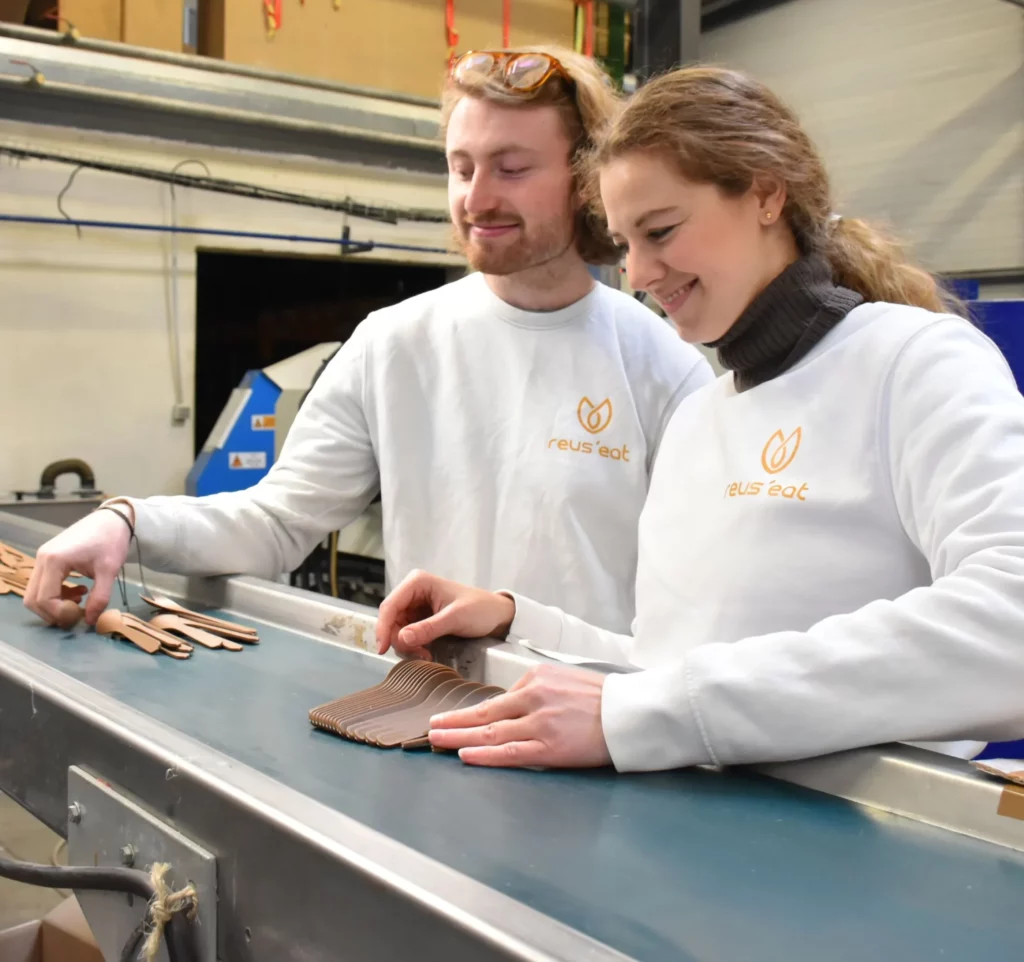 Fondateurs de Reus'eat (Marie Nagy et Armand Ferro) devant un tapis roulant industriel de leur production de kits de couverts de voyage français et naturels